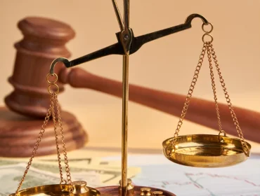 Balanza de justicia dorada sobre un fondo de documentos financieros y un mazo de juez, simbolizando la equidad en el sistema legal y la importancia de la justicia en asuntos económicos.